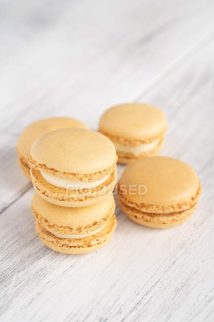 Orange tasty macaroons stacked in pile against wooden white surface — Stock Photo