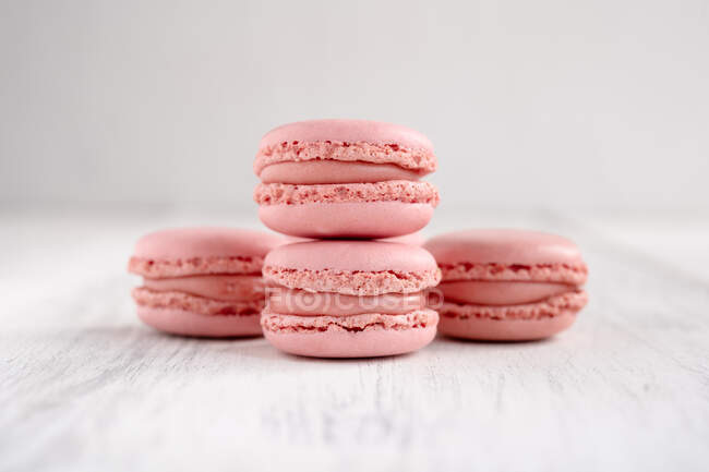 Pink tasty macaroons stacked in pile against wooden white surface — Stock Photo