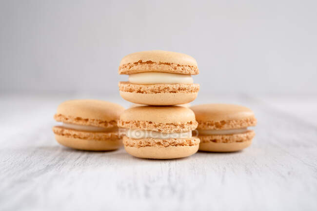Orange tasty macaroons stacked in pile against wooden white surface — Stock Photo