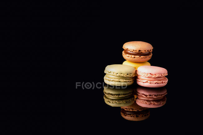 Macaroons saborosos coloridos empilhados exibidos no fundo preto — Fotografia de Stock