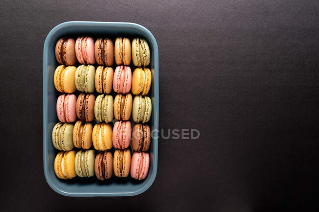 Macarons savoureux colorés affichés à l'intérieur conteneur bleu sur fond noir — Photo de stock