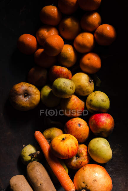Зверху свіжі соковиті яблука мандарин з гранатом і апельсиновою морквою на чорній поверхні у світлі — стокове фото