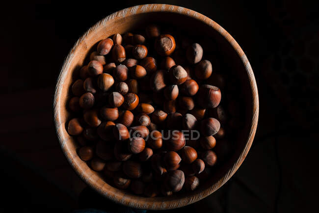 De cima tigela de madeira marrom cheia de avelã fresca saborosa no fundo preto — Fotografia de Stock