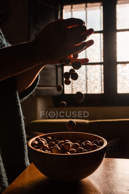Unrecognizable person grabbing full of tasty fresh hazelnut on brown wooden bowl — Stock Photo