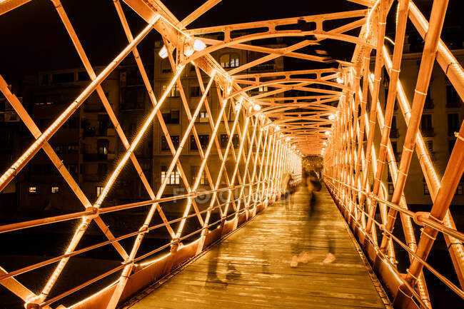 Construcción de puentes metálicos iluminados y personas caminando sobre puentes en Girona, Cataluña, España - foto de stock
