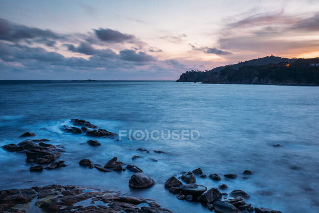 Smooth stones on shore of endless ocean washing island in cloudy day in Calella de Palafrugell, Costa Brava, Girona, Catalonia, Spain — Stock Photo