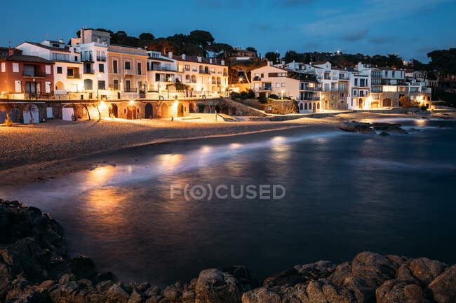 Crystal dark blue water reflecting lights on lantern on shore with architectural buildings in evening in Girona, Catalonia, Spain — Stock Photo