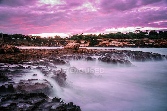 Mysterious landscape of empty rocky shore with fog under cloudy sky in lilac color — Stock Photo