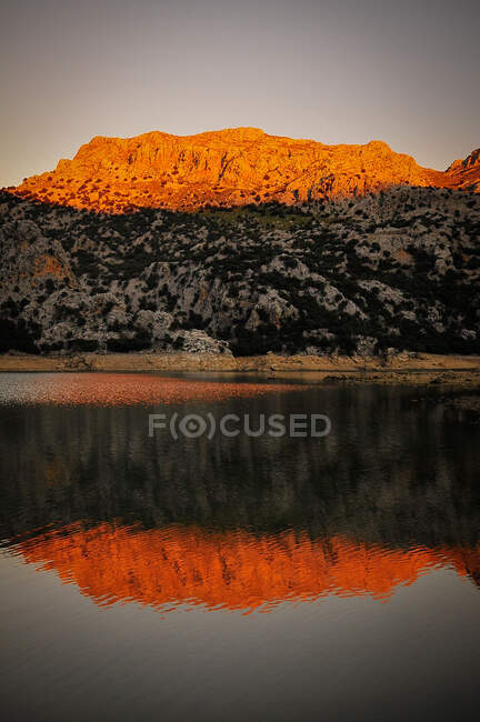 Helle bunte Landschaft aus orangefarbenem Gipfel und grauem Berg mit Bäumen bedeckt, umgeben von klarem Wasser, das Felsen reflektiert — Stockfoto