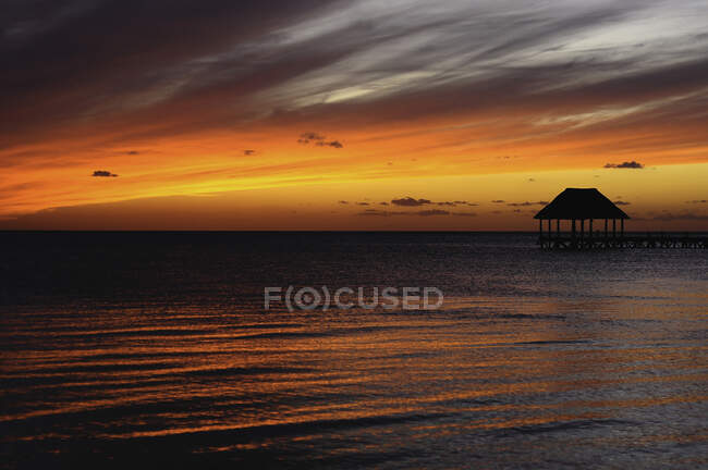 Breathtaking landscape of lonely pier with cabin in vast ocean under bright colorful sky in sunset — Stock Photo
