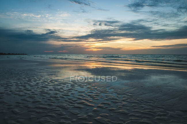 Calma tranquillo paesaggio marino di spiaggia vuota e oceano ondulato sotto cielo nuvoloso blu con luce solare arancione in cupo d ay — Foto stock