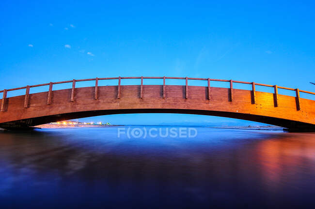 Einwandfreie Landschaft der antiken Konstruktion einer Holzbrücke über klares Wasser, das den blauen Himmel im Abendlicht reflektiert — Stockfoto