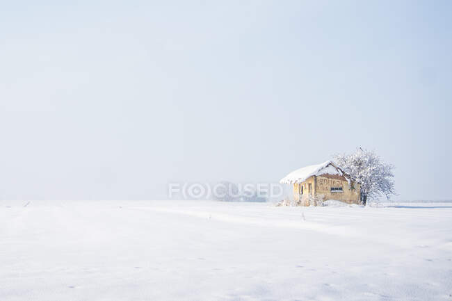 Білий пейзаж самотнього маленького будинку зі сніговим дахом у порожній гладкій білій долині під нескінченним небом — стокове фото