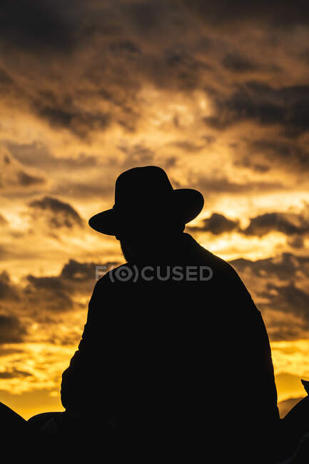 Rückansicht der nicht erkennbaren Silhouette eines Mannes, der auf dem Dach des Gebäudes sitzt und den Blick auf den Sonnenuntergang der Stadt schweifen lässt — Stockfoto