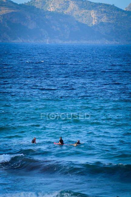 Grupo de surfistas en tablas en el mar contra montañas esperando a que la ola cabalgue en un día soleado - foto de stock