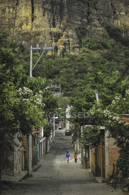 Maman et enfant marchant dans la rue de la ville âgée contre la haute falaise couverte de verdure — Photo de stock