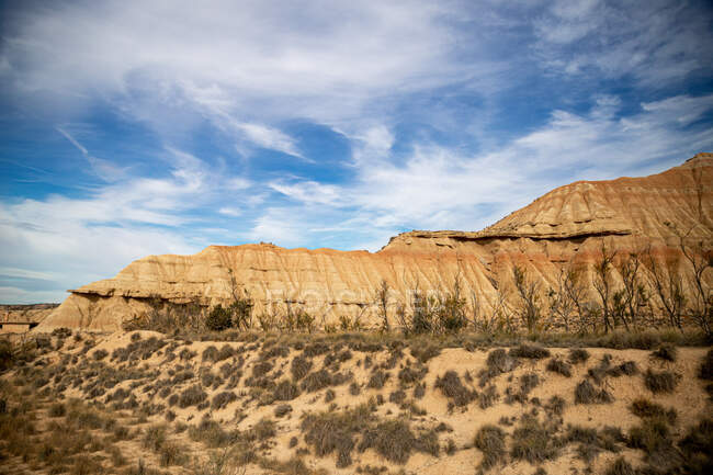 Empty field with green sparse vegetation and brown powerful cliff on background under cloudy blue sky in Bardenas Reales, Navarre, Spain — Stock Photo