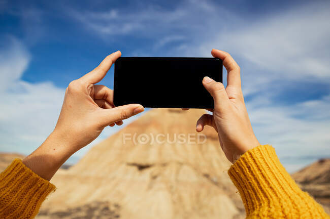 Frauenhände eines anonymen Reisenden beim Fotografieren einer großen braunen Klippe mit buntem blauen Himmel und weißen Wolken auf dem Hintergrund bei Bardenas Reales in Spanien — Stockfoto