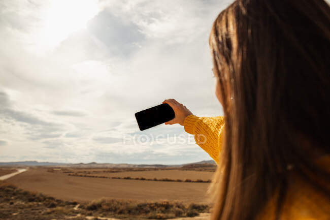 Vista posteriore di viaggiatrice anonima in elegante abbigliamento casual scattare selfie sul telefono cellulare nel deserto a Bardenas Reales, Navarra, Spagna — Foto stock