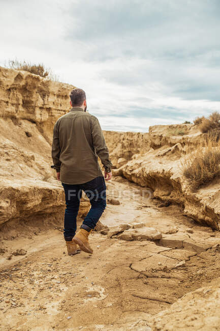 Visão traseira do viajante masculino sem rosto em roupas casuais em passagem estreita entre grandes pedras marrons em Bardenas Reales, Navarra, Espanha — Fotografia de Stock