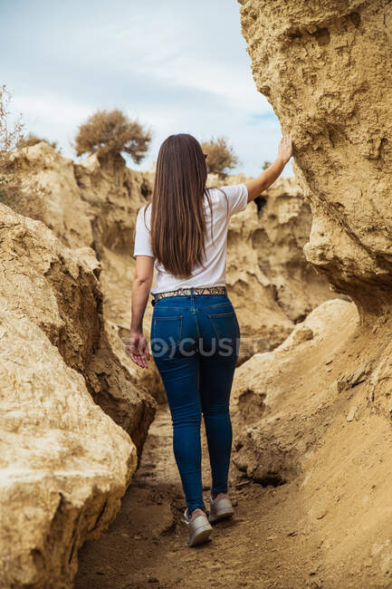 Vista posterior de una viajera sin rostro vestida con ropa casual en estrecho pasaje entre grandes piedras marrones en Bardenas Reales, Navarra, España - foto de stock