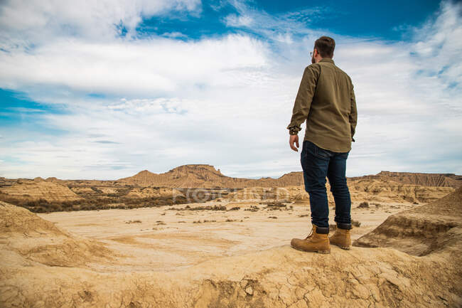 Visão traseira do homem anônimo em uso casual descansando na montanha marrom com céu azul no fundo em Bardenas Reales — Fotografia de Stock
