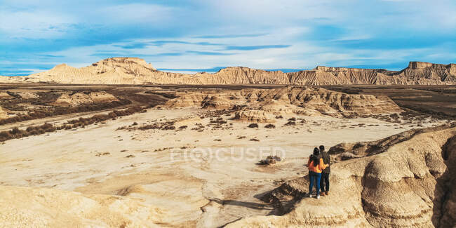 From above of couple on vacation standing on edge and cliff in an embrace and kissing with deserted landscape and blue sky on background in Bardenas Reales, Navarre, Spain — Stock Photo