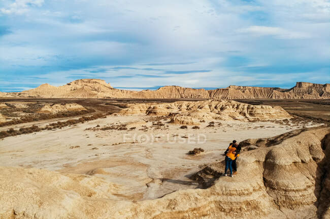 From above of couple on vacation standing on edge and cliff in an embrace and kissing with deserted landscape and blue sky on background in Bardenas Reales, Navarre, Spain — Stock Photo