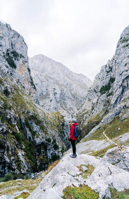 Vista lateral do caminhante mulher ativa em casaco vermelho com mochila pesada olhando para a montanha em picos da Europa, Astúrias, Espanha — Fotografia de Stock