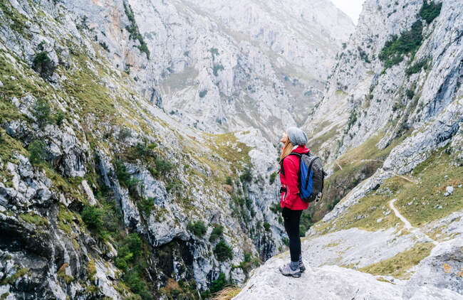 Vista lateral do caminhante mulher ativa em casaco vermelho com mochila pesada olhando para a montanha em picos da Europa, Astúrias, Espanha — Fotografia de Stock
