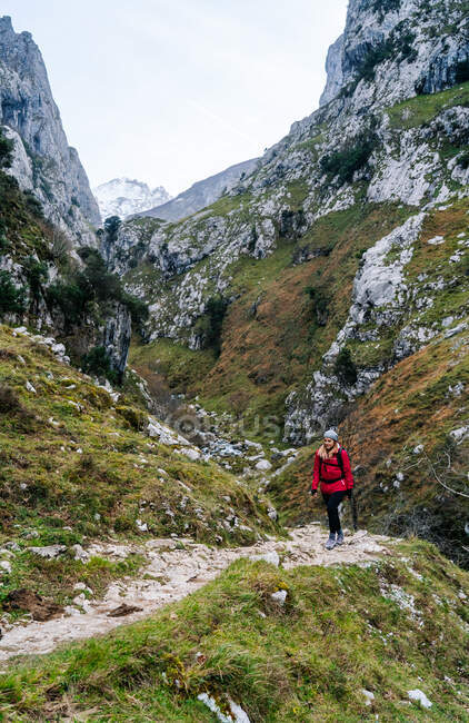 Active woman hiker in red jacket with heavy backpack looking at camera while walking in mountain in peaks of Europe, Asturias, Spain — Stock Photo