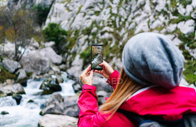 Bright photo of mountain waterfall and turquoise lake flowing into river on smartphone in hand of crop unrecognizable woman tourist in peaks of Europe, Asturias, Spain — Stock Photo