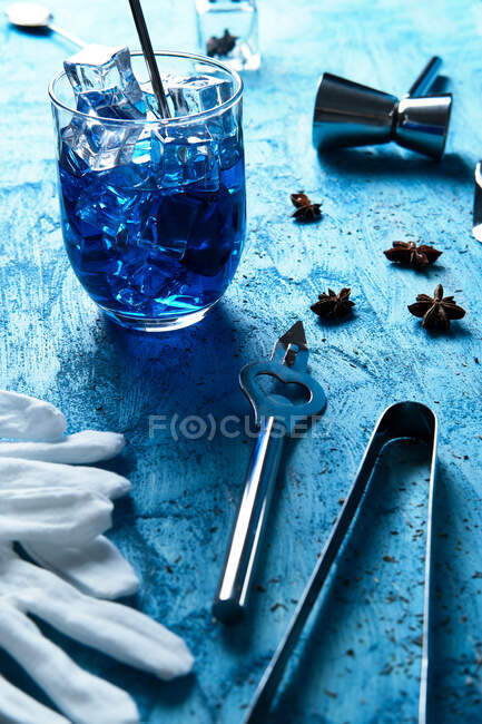 From above fresh blue cocktail with ice cubes and barman equipment with gloves on blue table — Stock Photo