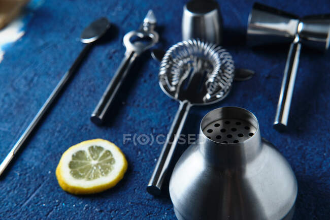From above professional stainless steel set of barman equipment and lemon slice on blue counter — Stock Photo