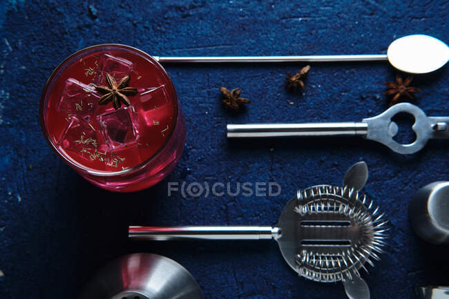 Вид зверху на смачний червоний напій з кубиками льоду та набором барменів на синьому столі — стокове фото