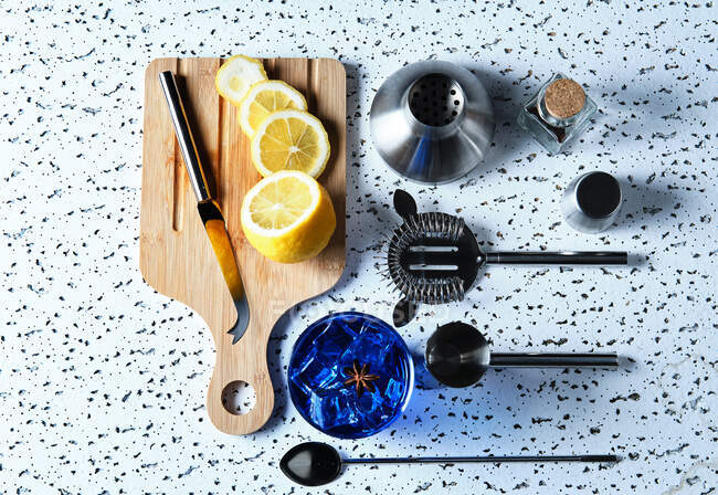 Vue de dessus du cocktail bleu avec glaçons et citron tranché sur une planche en bois avec des outils de barman sur la table — Photo de stock