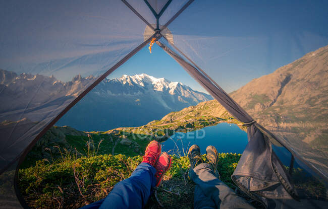 Ernte angenehme Wanderer in bunten Turnschuhen liegen mit überkreuzten Beinen in einem kleinen transparenten Zelt in der Nähe des klaren Sees in den Bergen bei sonnigem Tag in Chamonix, Mont-Blanc — Stockfoto
