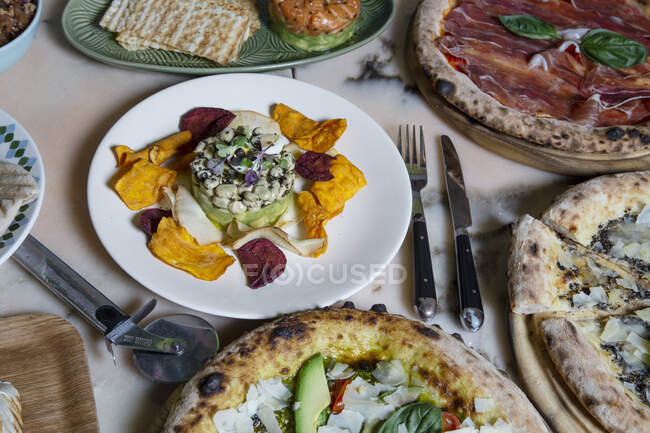 De cima do prato de feijão com pétalas na chapa perto de garfo com faca e pizza na mesa — Fotografia de Stock