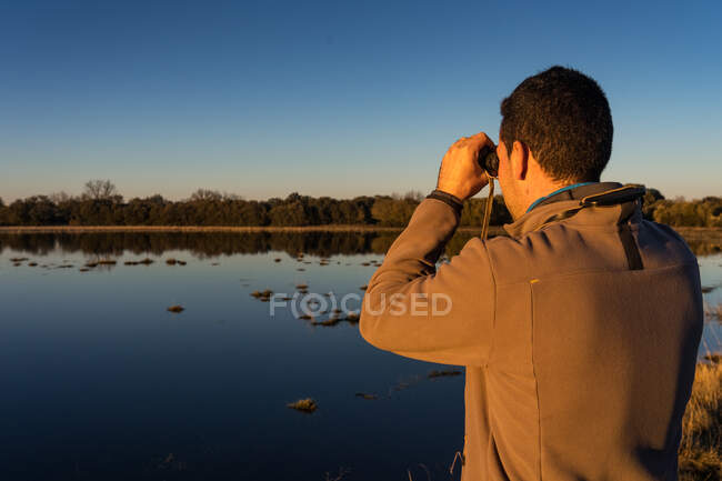 Visão traseira do homem irreconhecível olhando através de um binóculos velhos a fauna de uma lagoa na Espanha — Fotografia de Stock