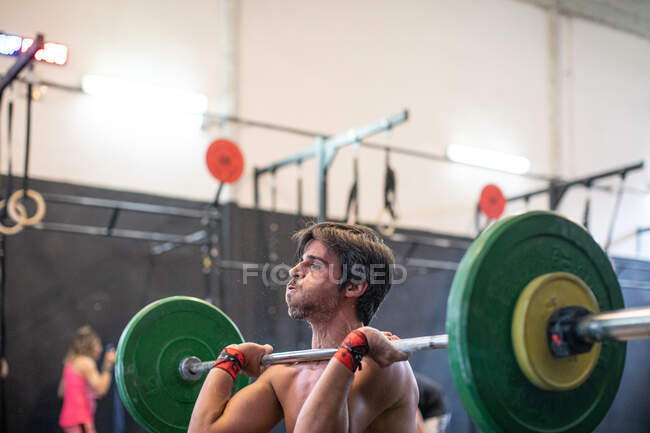 Muscular cara levantando barbell no ginásio moderno — Fotografia de Stock