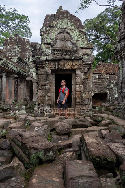 Unbekümmerter Mann mit Rucksack betrachtet historischen Ort, während er auf Ruinen des religiösen Tempels von Angkor Wat in Kambodscha steht — Stockfoto