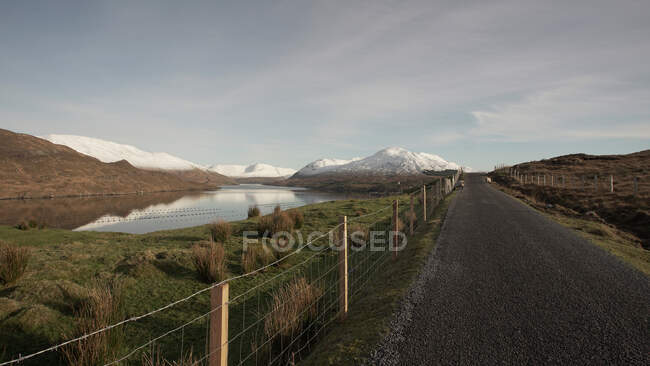 Paesaggio pittoresco di strada asfaltata con recinzione vicino al fiume e catene montuose in Irlanda — Foto stock