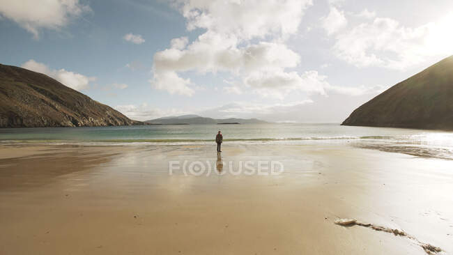 Uomo turistico contemplare calma natura paesaggio oceanico mentre in piedi sulla spiaggia di sabbia sulla costa d'Irlanda — Foto stock