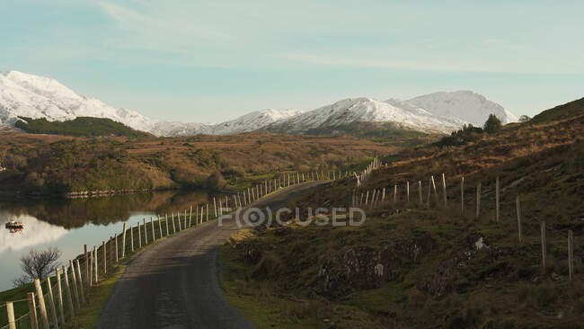 Malerische Landschaft der Asphaltstraße mit Zaun in der Nähe von Fluss und Gebirge in Irland — Stockfoto