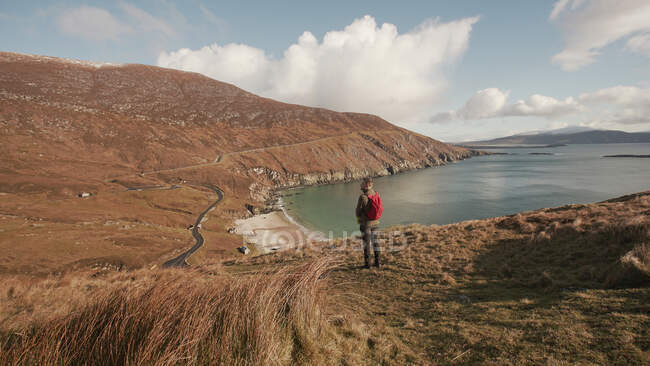 Беззаботный человек наслаждается прекрасным природным ландшафтом и морем, стоя на скале в Ирландии, глядя в сторону — стоковое фото