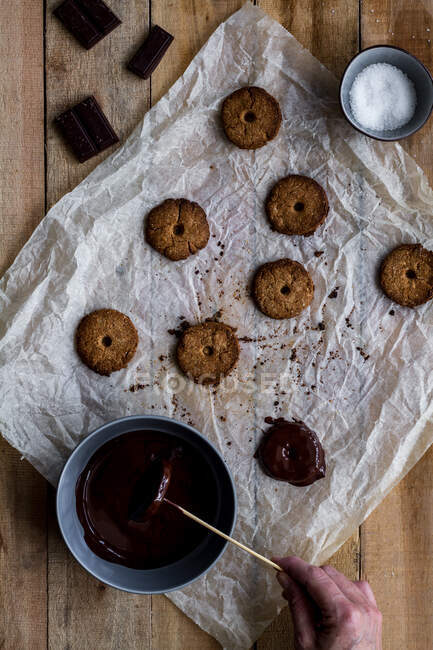 De la culture ci-dessus cuisinier anonyme verser des biscuits savoureux cuits au four avec du sirop de chocolat dans du papier cuisson sur une table en bois — Photo de stock