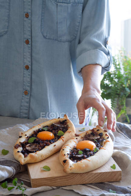 De acima mencionado cozinheiro de cultura polvilhando com verdes recém-preparados kachapuri com ovos apetitosos em suporte de madeira na mesa — Fotografia de Stock