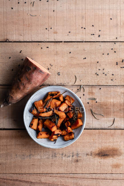 Vista dall'alto di mezza patata dolce cruda e pezzi di patata dolce al forno in ciotola su tavolo rustico in legno — Foto stock