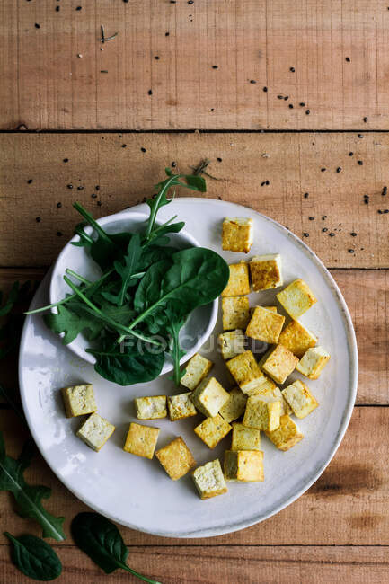 Top view of green basil leaves and cubes of cheese on plate on wooden rustic table — Stock Photo