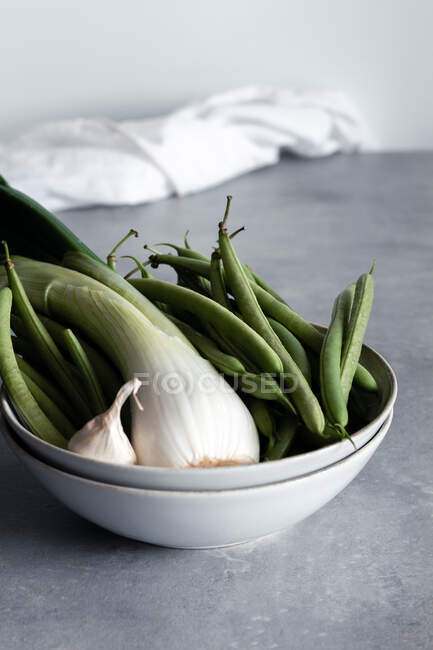 Weiße Schüssel mit Knoblauch und grünen Zwiebeln und grünen Bohnen auf dem Tisch in der Küche — Stockfoto